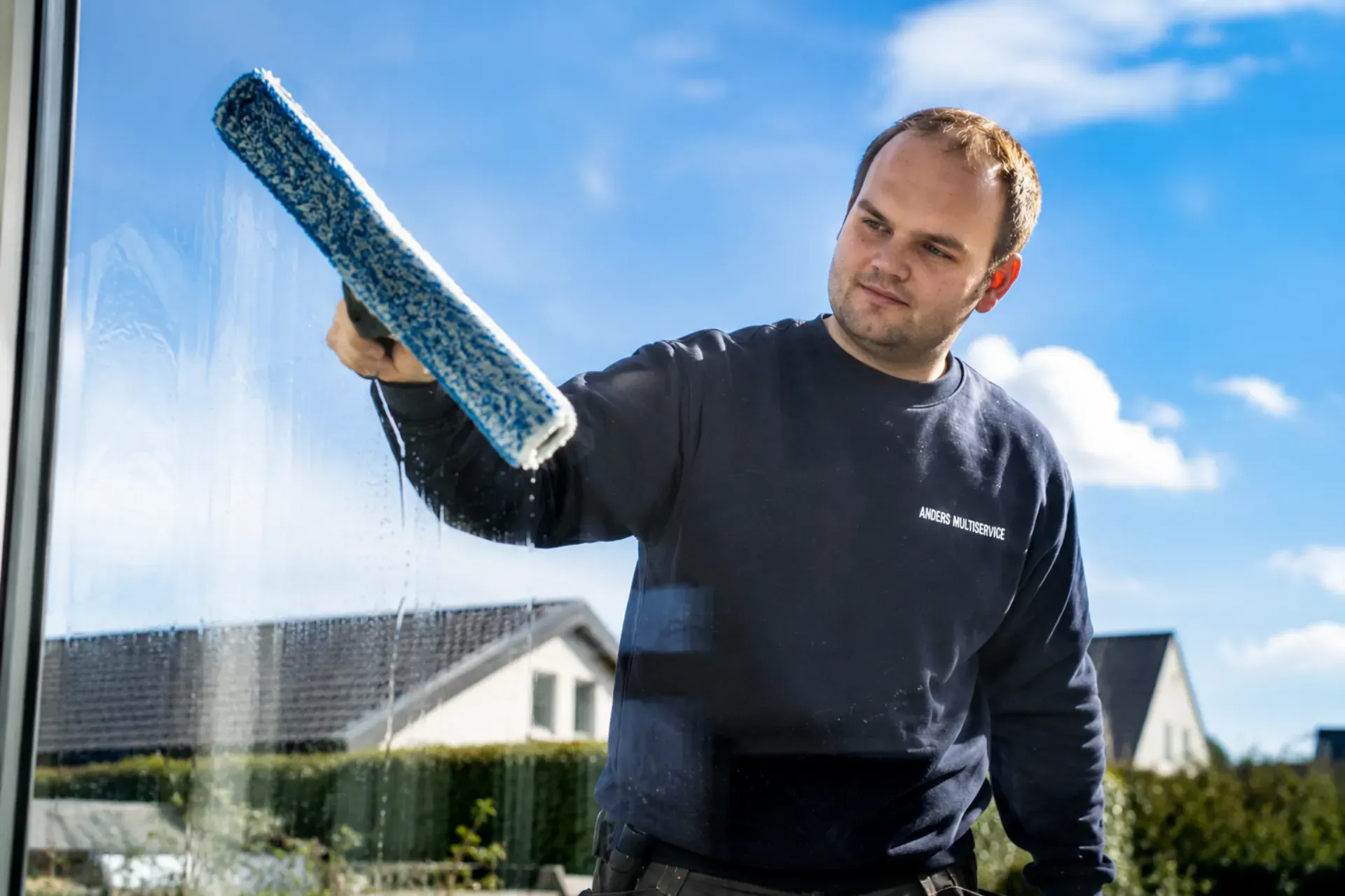 Mand vasker vindue med skuresvamp i solrigt vejr.